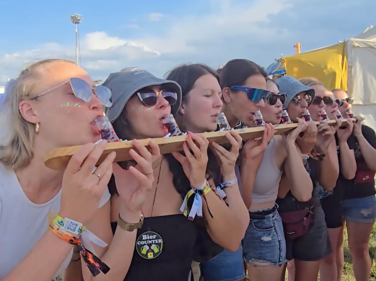 Gruppe mit Festivalbändern trinkt gemeinsam vom langen Shotski am Campingplatz