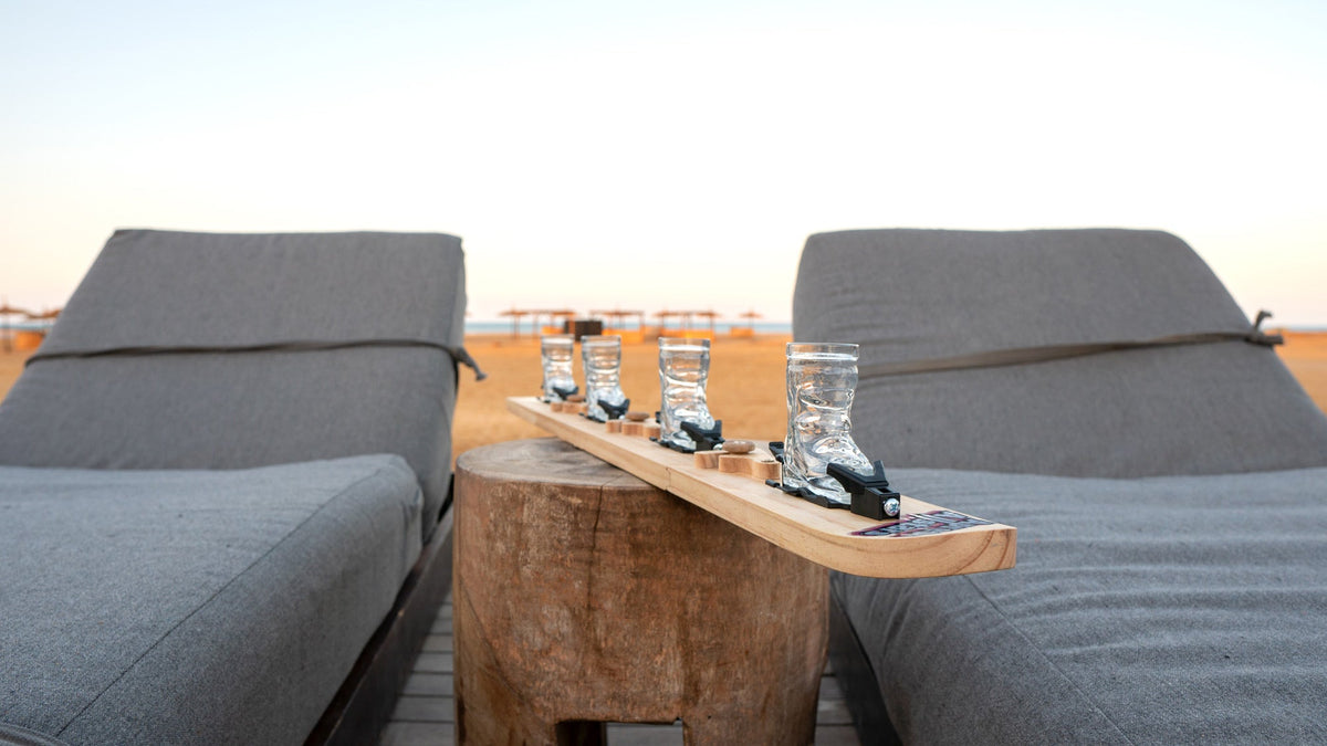 Shotski mit vier Skischuh-Gläsern zwischen zwei Liegen am Strand, bereit fürs Vorglühen