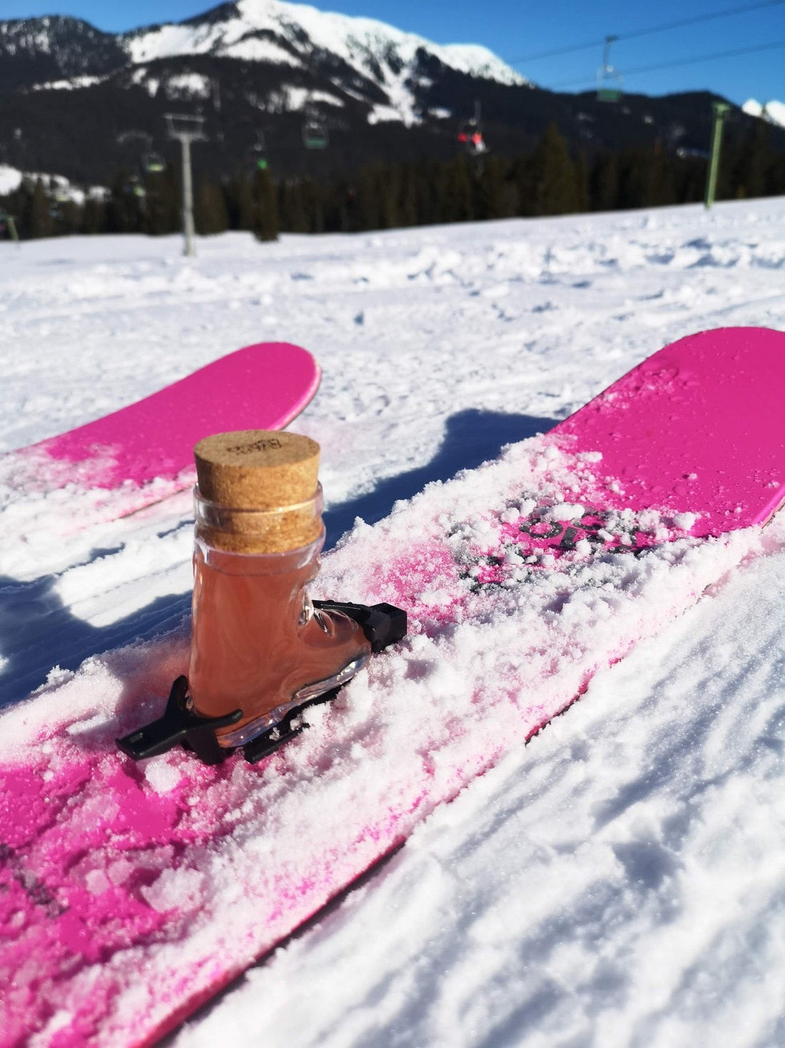 Skischuh-Shotglas mit Korken und Bindung auf einem pinken Ski im Schnee
