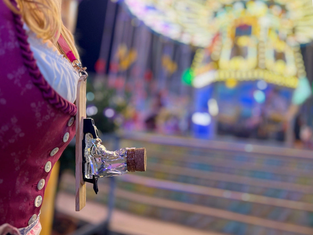 Frau im Dirndl mit Schnapsglas am Band vor einem beleuchteten Fahrgeschäft