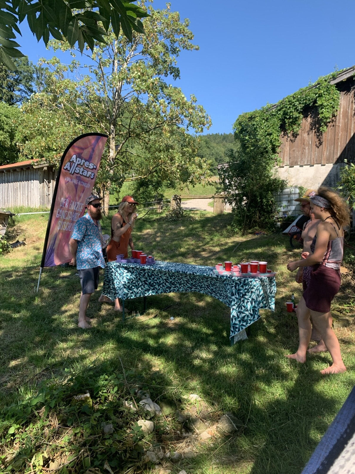 Gartenparty auf der Wiese mit Apres-Allstars-Fahne und Bechern — lustige Spiele fuer draussen