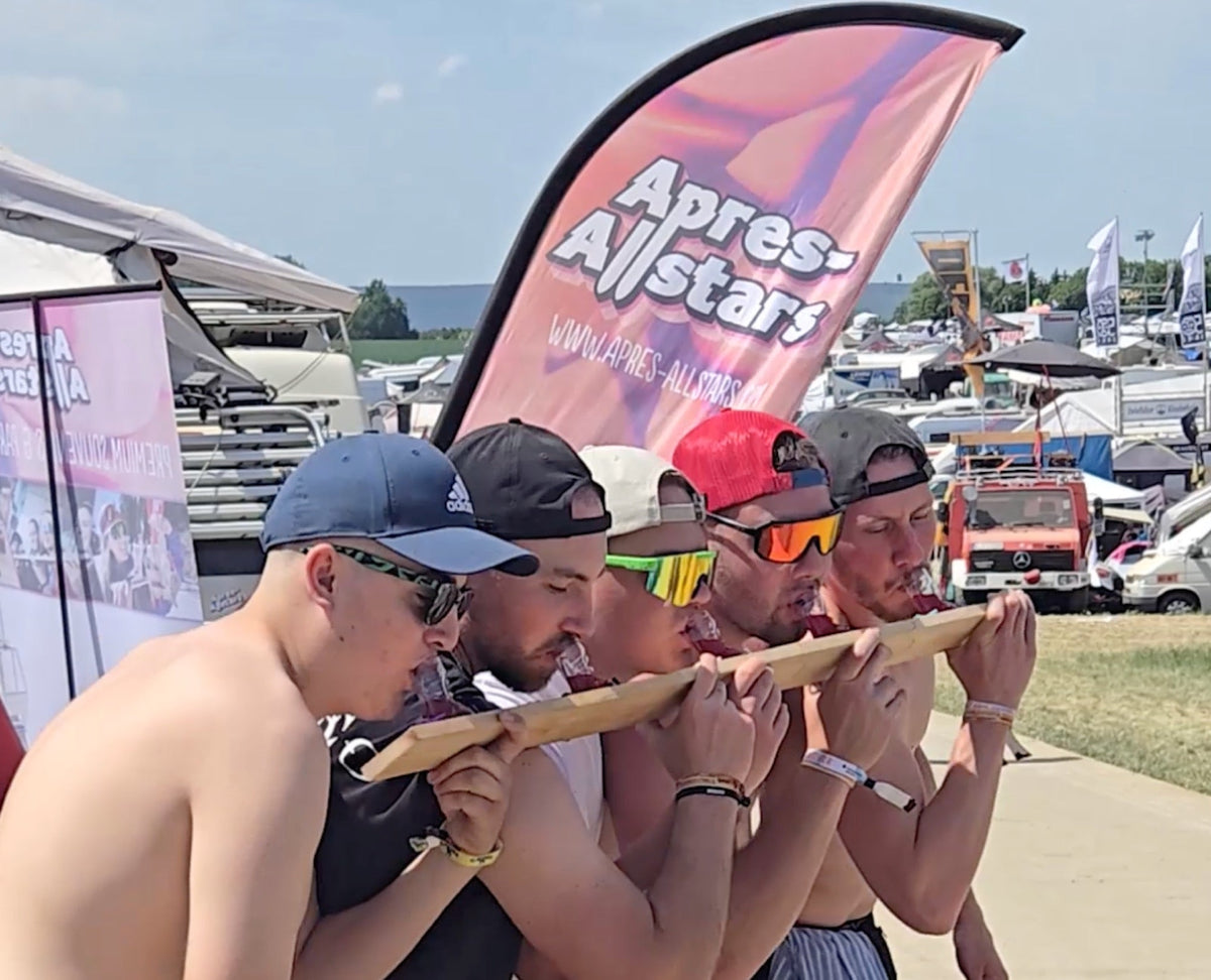 Fünf Festivalbesucher trinken vom SwigSki3000 Shotski vor dem Apres-Allstars-Banner