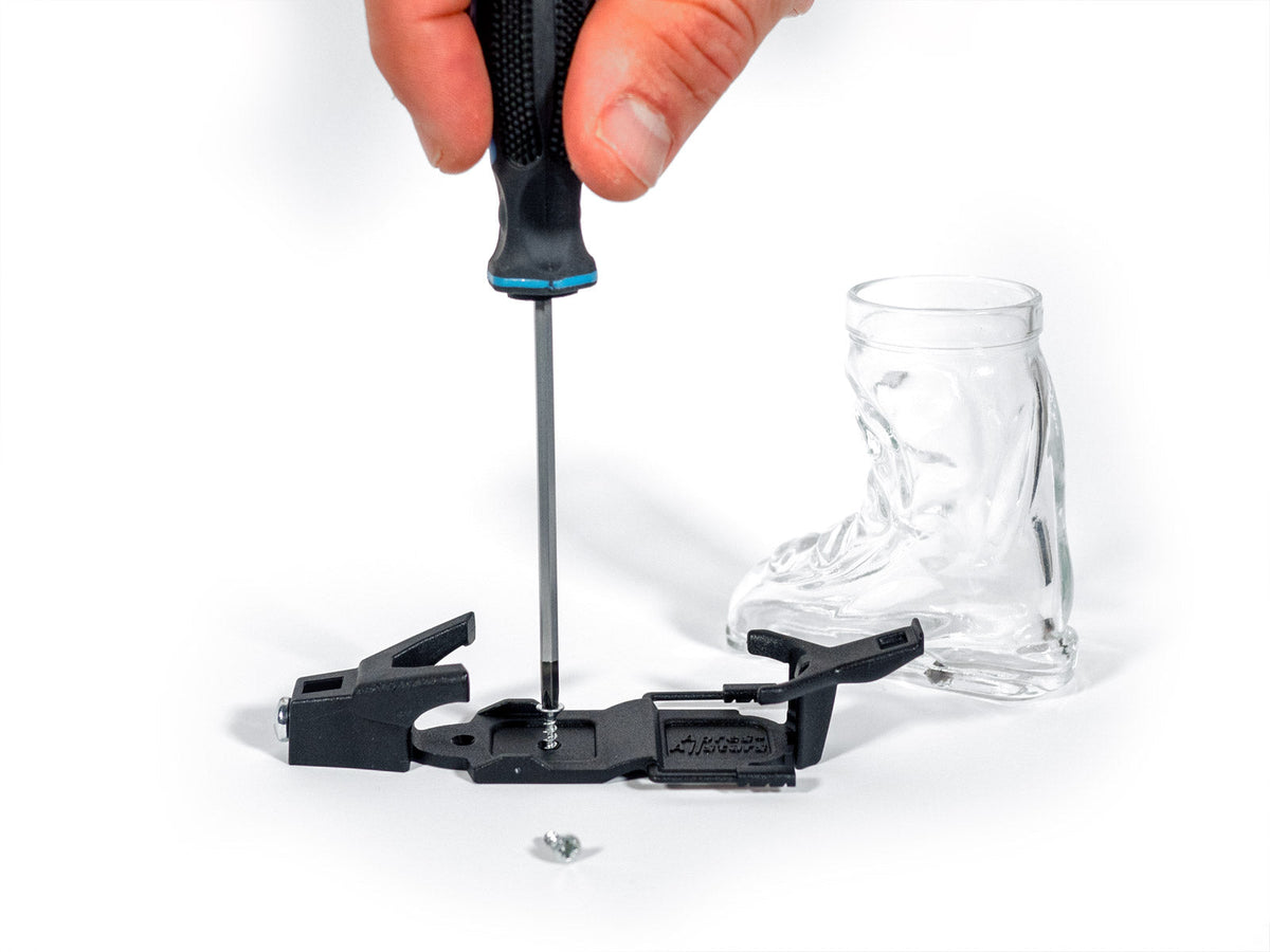 Skischuh-Glas-Bindung wird mit einem Schraubenzieher montiert, daneben das Schnapsglas