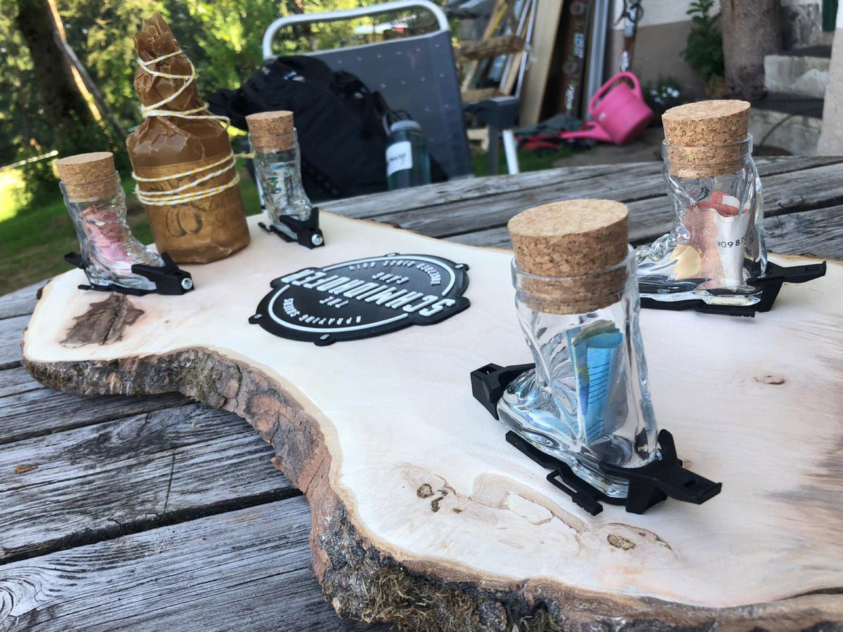 Skischuh-Schnapsgläser mit Geldscheinen gefüllt auf einem Holzbrett im sommerlichen Garten