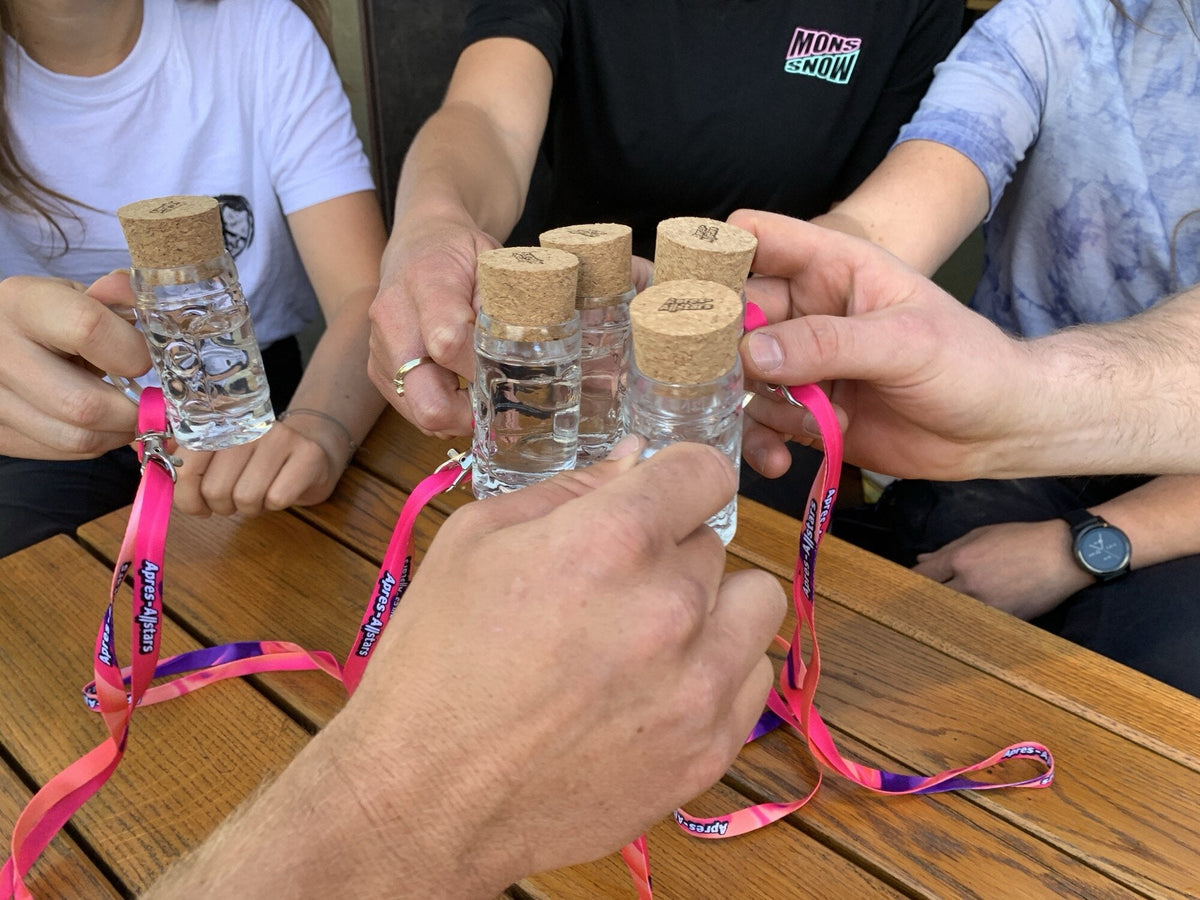 Gruppe stößt an einem Holztisch mit kleinen Schnapsfläschchen und pinken Lanyards an