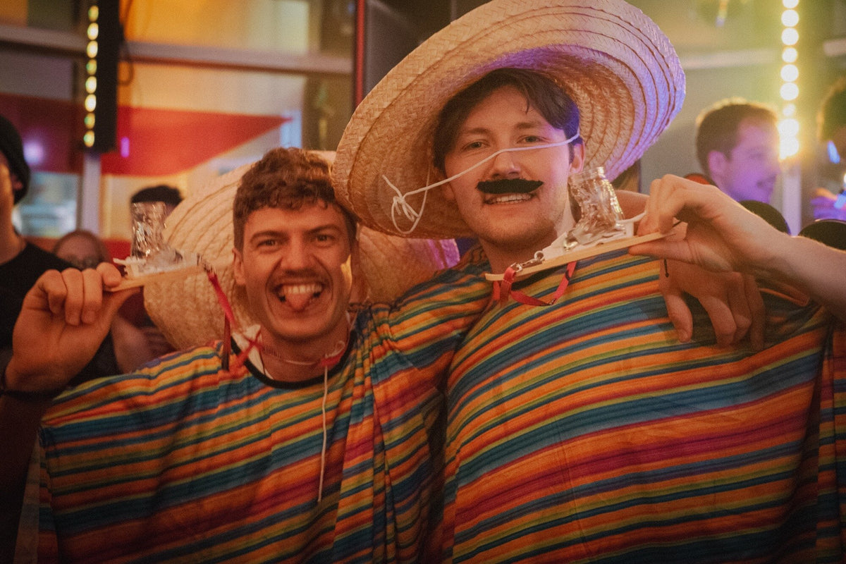 Zwei Partygäste in Ponchos und Sombreros lachen mit dem Apres-Allstars-Shotski