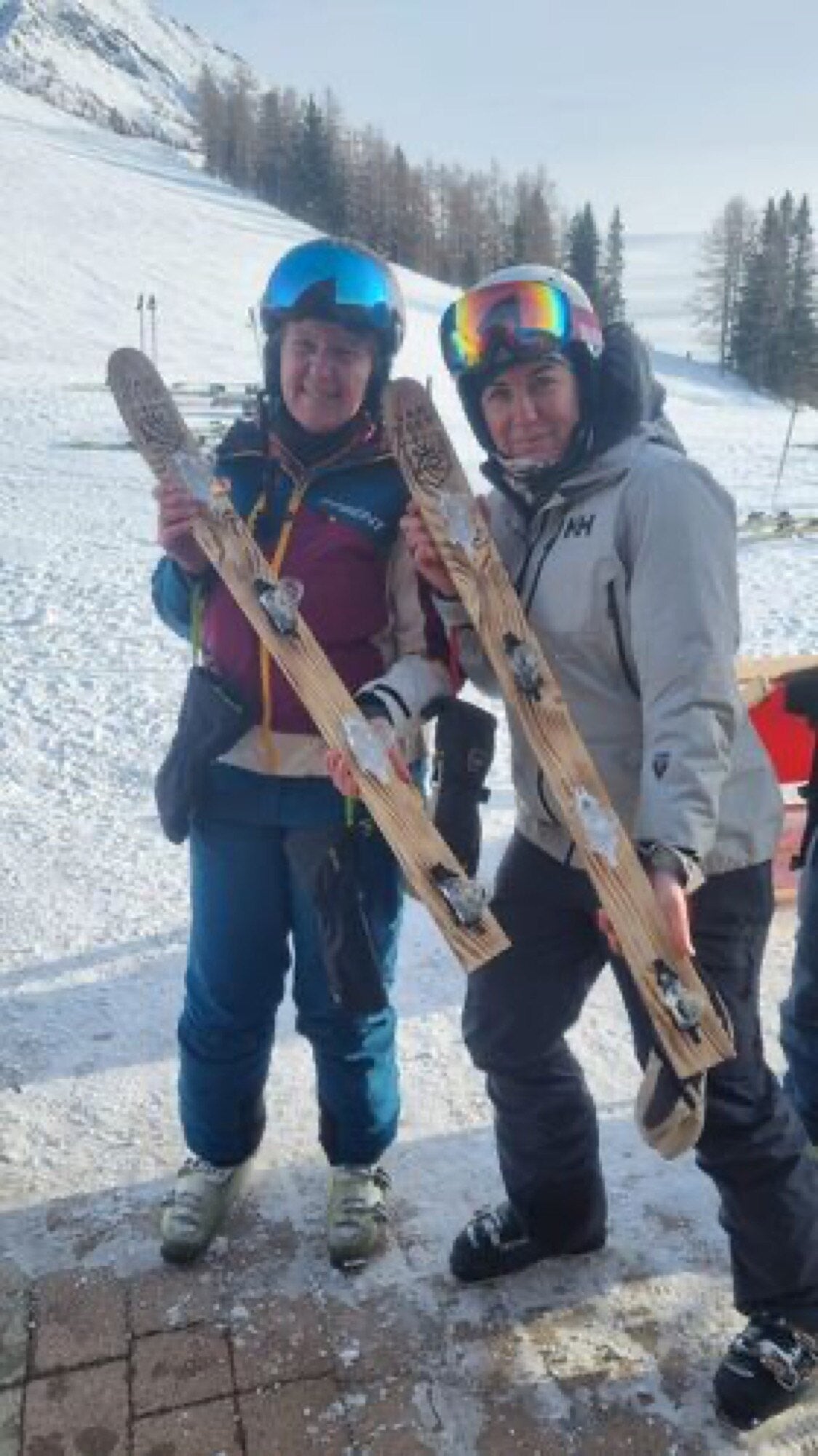 Zwei lachende Frauen mit Skihelmen halten Holz-Schnaps-Skier im Schnee — Wahrheit oder Pflicht ab 16