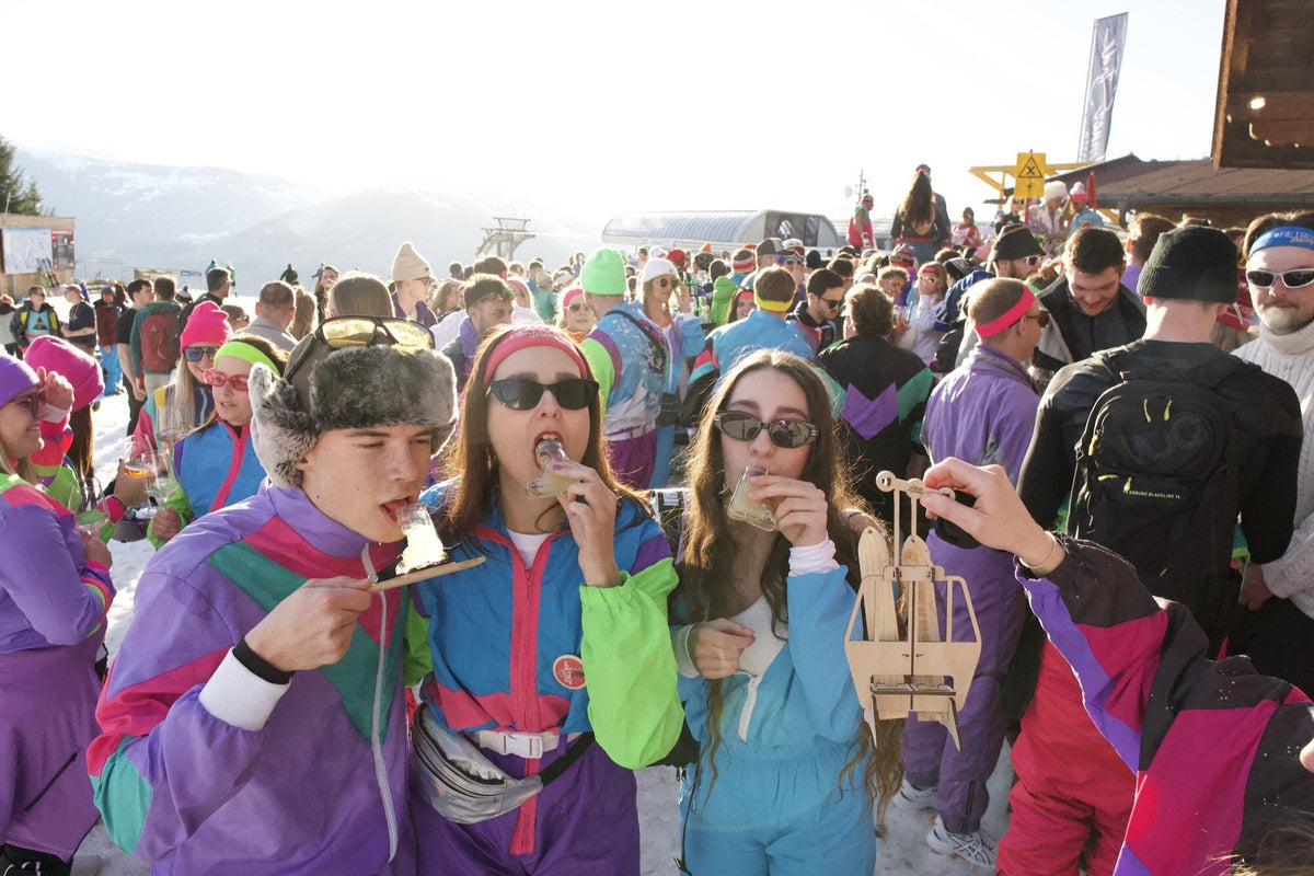 Drei junge Frauen in Retro-Skioutfits trinken aus Miniski-Glaesern — Wahrheit oder Pflicht Maedelsabend