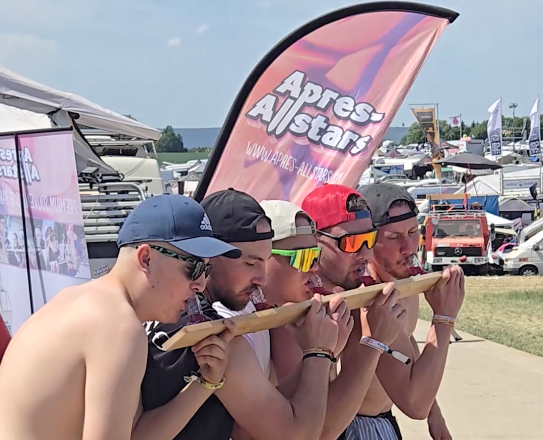 Fünf Festivalbesucher trinken vom SwigSki3000 Shotski vor dem Apres-Allstars-Banner